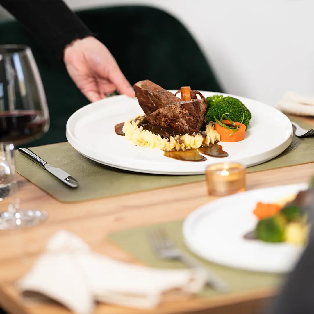 Vorspeiseteller mit geschmortem Rinderbraten auf Kartoffelpüree, Karottenrolle und Brokkoli, serviert auf weißem Teller am Tisch im Lopshof